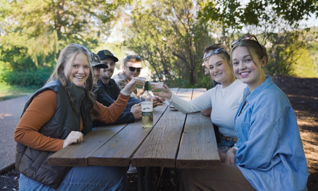 Friends sharing a bottle of Stone Hill wine at a picnic table on the hillside during Oktoberfest