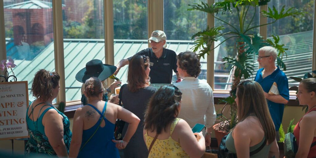 Guests gathered around a host pouring wine in the glass-walled Conservatory