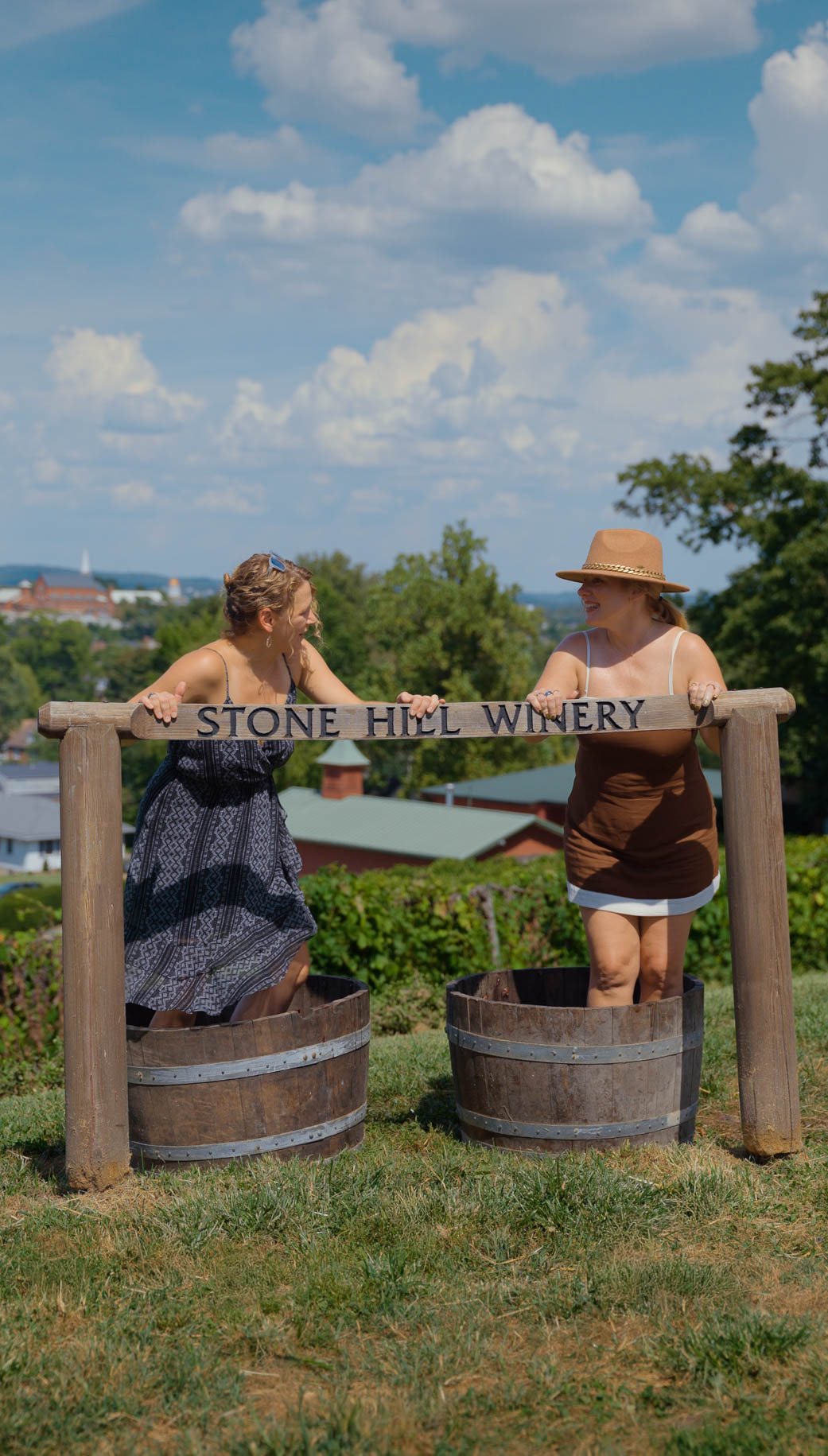 Two women laughing as they stomp grapes in barrels under the Stone Hill Winery sign