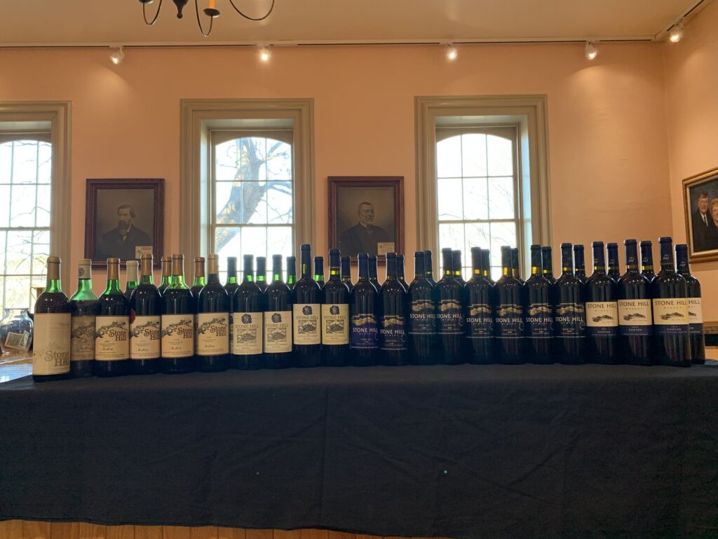 A long row of Stone Hill Norton bottles from many vintages on a table in a historic room