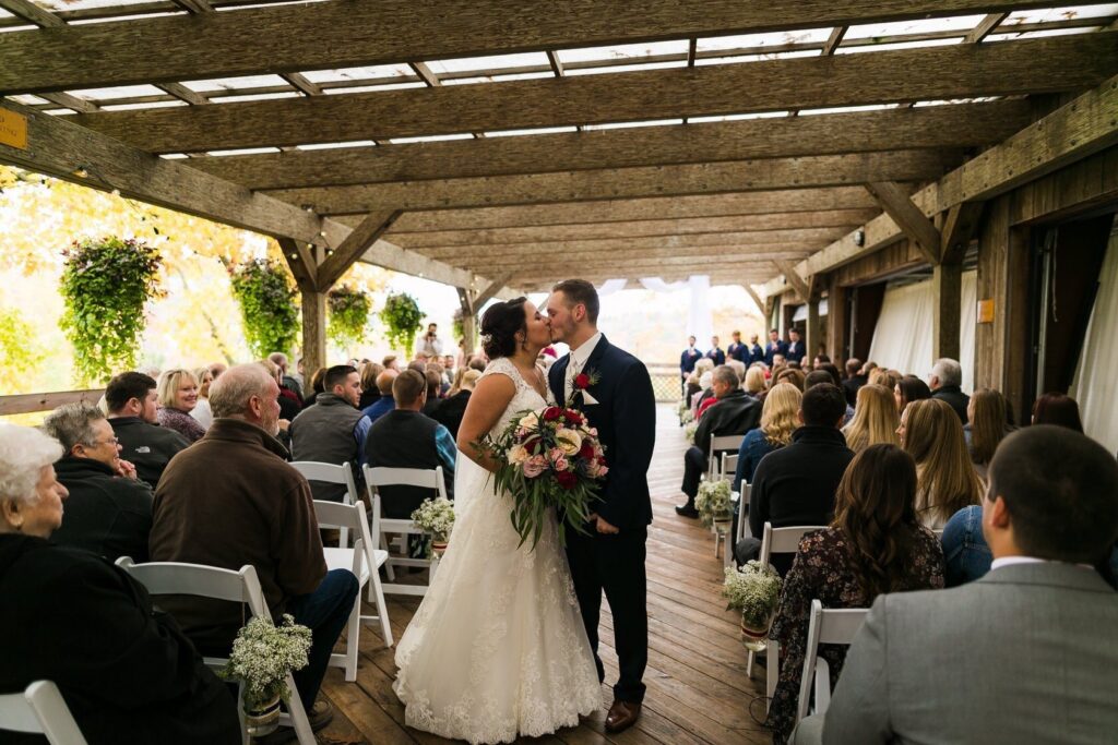 Bride and groom kissing at the end of the aisle on the Sherry House deck as guests look on